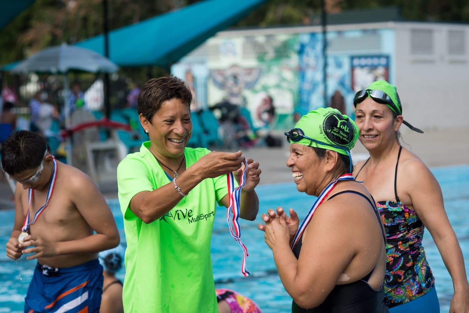 A ViVe coach in a lime shirt places a medal on a smiling young swimmer